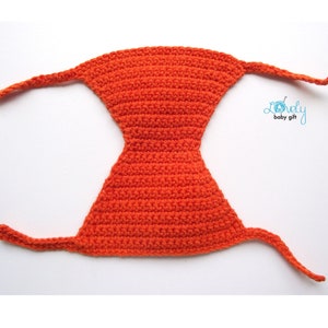 May include: Bright orange crocheted baby bonnet with long ties. The bonnet is a solid color and has a unique shape. The text "Lovely baby gift" is in the upper right corner.