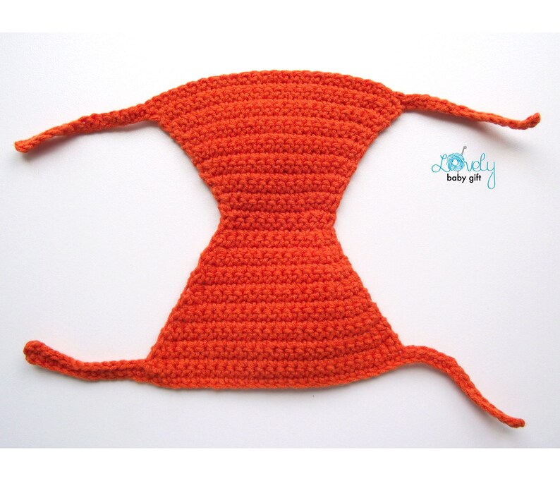 May include: Bright orange crocheted baby bonnet with long ties. The bonnet is a solid color and has a unique shape. The text "Lovely baby gift" is in the upper right corner.