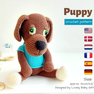 Könnte beinhalten: Ein gehäkelter brauner Welpe mit schwarzer Nase, grünen Augen und einem blauen Hemd. Der Welpe ist etwa 32 cm groß. Das Bild enthält den Text "Puppy crochet pattern".