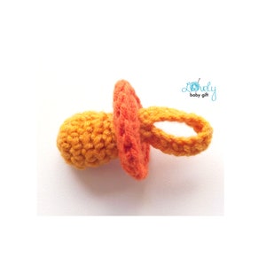 May include: A handmade crochet baby pacifier in shades of orange and yellow. The pacifier features a round nipple, a circular shield, and a loop for easy handling. The text "Lovely baby gift" is in the upper right corner.