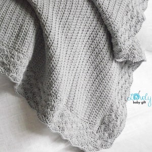 May include: A gray crocheted baby blanket with a scalloped edge and a delicate floral pattern. The blanket is made with soft yarn and is perfect for cuddling.