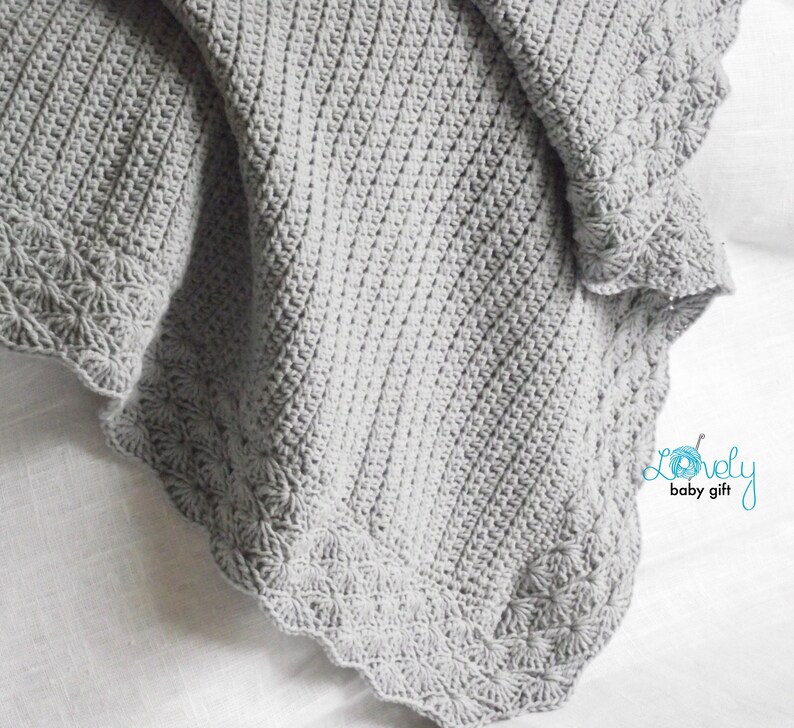 May include: A gray crocheted baby blanket with a scalloped edge and a delicate floral pattern. The blanket is made with soft yarn and is perfect for cuddling.