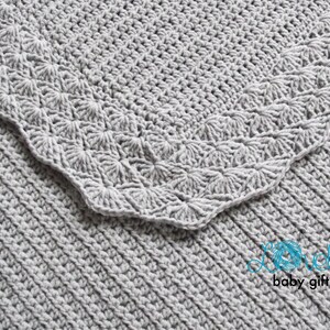 May include: A gray crocheted baby blanket with a scalloped border. The blanket is made with a textured stitch and has a delicate, feminine look.