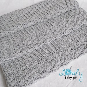 May include: A gray crocheted baby blanket with a decorative border. The blanket is folded in thirds and has a subtle texture.