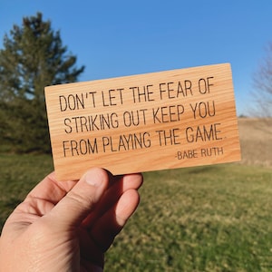 May include: A wooden sign with the quote "Don't let the fear of striking out keep you from playing the game." attributed to Babe Ruth.