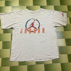 Puede incluir: Camiseta blanca con el logo de Jordan en rojo, naranja y azul. El logo muestra la silueta de un jugador de baloncesto en el aire, con la palabra "JORDAN" debajo. Peque&ntilde;o logo de Nike en la manga.