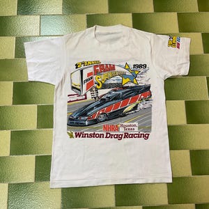 May include: White t-shirt featuring a drag racing car graphic with red and black accents. The shirt includes the text "2nd Annual FRAM Supernationals 1989" and "Winston Drag Racing" with the NHRA logo.