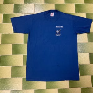 May include: A royal blue t-shirt with short sleeves. The shirt features the text "Mackinaw City" and the WWF logo in white. The shirt is made of a soft material and is likely vintage.