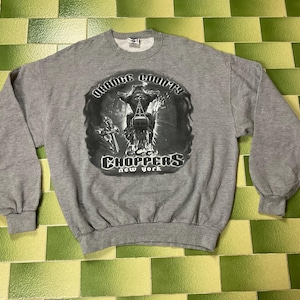 May include: A gray sweatshirt featuring a graphic of a motorcycle and rider, with the text "Orange County Choppers New York" in a circular design. The sweatshirt has long sleeves and a crew neck.