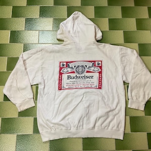 May include: White hooded sweatshirt with the Budweiser logo on the back. The logo is a red and white rectangle with the Budweiser name and other text. The sweatshirt has long sleeves and a hood.