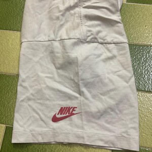Puede incluir: Una secci&oacute;n de pantalones cortos deportivos blancos con el logo rojo de Nike. Los pantalones cortos tienen una costura en el centro y un panel de tela contrastante en la parte inferior. La tela parece ligera.
