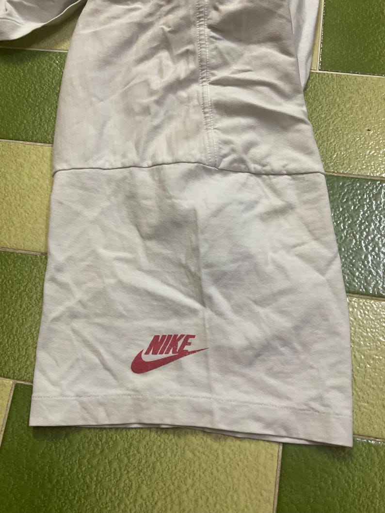 Puede incluir: Una secci&oacute;n de pantalones cortos deportivos blancos con el logo rojo de Nike. Los pantalones cortos tienen una costura en el centro y un panel de tela contrastante en la parte inferior. La tela parece ligera.
