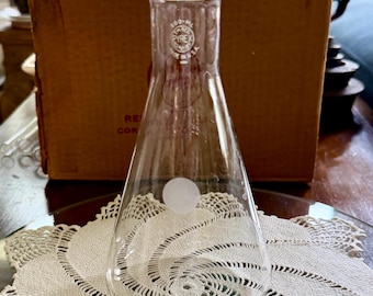 May include: A clear glass Erlenmeyer flask with a 500-ml capacity marking and the Pyrex brand logo printed in white on the neck. The flask features a conical body, a narrow cylindrical neck with a flared rim, and a small white circular marking.