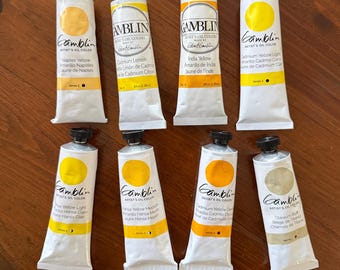 May include: Eight tubes of Gamblin Artist's Oil Color in various shades of yellow and beige. Each tube is white with a yellow label and black cap. The labels include the color name in English, Spanish, and French.