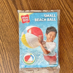 May include: A packaged small beach ball with red, white, and yellow panels. The packaging features the text "Play Day" and "Small Beach Ball", along with an illustration of a child holding the ball. Ages 2+.