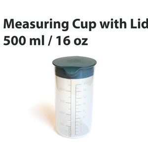 May include: A clear plastic measuring cup with a green lid. The cup has markings for milliliters and ounces. It is labeled "500 ml / 16 oz".