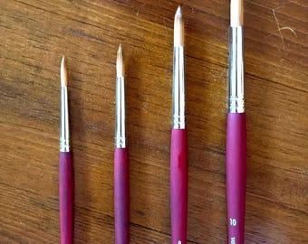 May include: Four Princeton Velvetouch paint brushes with maroon handles and silver ferrules, arranged by size. Each brush features a pointed tip and is labeled with the brand name and size numbers 4, 6, 8, and 10 printed in white on the handle.