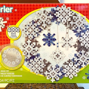 May include: A Perler fused bead kit box featuring a wreath made of white, light blue, and dark blue snowflake designs. The packaging displays 4000 beads, a circular pegboard, and three hanging snowflake ornaments in shades of blue and white.