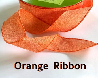May include: A close-up of a bright orange ribbon with a textured woven fabric. The ribbon is folded and curled, showing its soft and pliable texture.