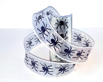 May include: A spool of translucent white ribbon featuring a repeating pattern of black spider silhouettes. The ribbon has a wired edge and is coiled in a loose loop, displaying the dark arachnid graphics clearly against the sheer fabric material.