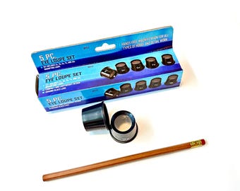 May include: A set of 5 magnifying eye loupes in a blue and white box. The loupes are black and come in different magnifications: 2x, 3x, 5x, 7x, and 10x. The box says "Hands-free magnification for all types of hobby and detail work."