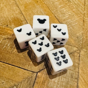 May include: Five white dice with black bear-shaped pips. The dice are arranged on a wooden surface. Each die has a different number of bear pips, ranging from one to six.