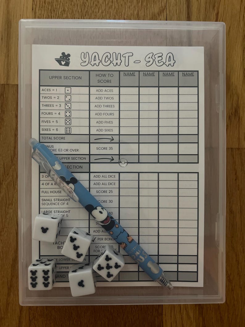 May include: A clear plastic case containing a Yacht-Sea game set. The set includes a score sheet, dice, and a Mickey Mouse-themed pen. The dice are white with black Mickey Mouse icons. The score sheet has the game's title and scoring sections.