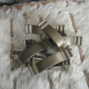 May include: A set of five antique-style, brushed brass cabinet pulls with a decorative, wavy design. The pulls are arranged in a pile on a white, furry surface.