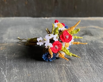 May include: A crocheted bouquet of flowers in red, white, yellow, and blue. The bouquet includes poppies, daisies, and other small flowers.