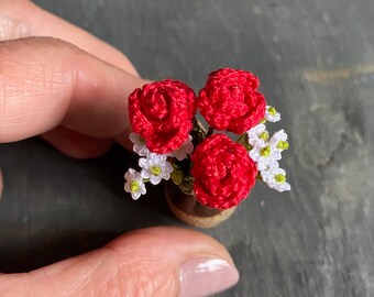 May include: A small crocheted bouquet of red roses with white flowers in a brown pot.