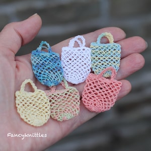 May include: Six small crocheted mesh bags in various colors, including blue, white, yellow, pink, and green. The bags are displayed in a hand, with the text "Fancyknittles" visible at the bottom of the image.
