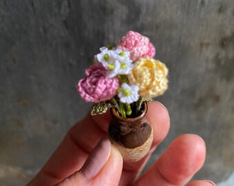 May include: A small bouquet of crocheted flowers in pink, white, and yellow, arranged in a brown ceramic vase. The flowers are delicate and detailed, with a realistic appearance.