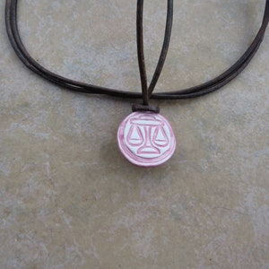 May include: A brown leather cord necklace with a pink and white ceramic pendant featuring a scale design.