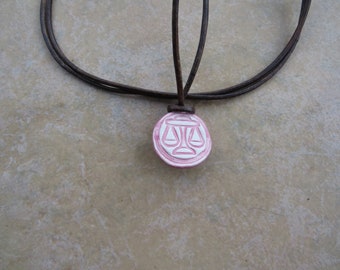 May include: A brown leather cord necklace with a pink and white ceramic pendant featuring a scale design.