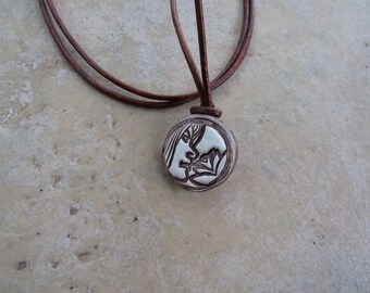 May include: A brown leather cord necklace with a round ceramic pendant featuring a white silhouette of two people kissing.