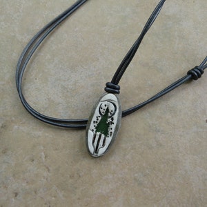 May include: A black leather cord necklace with an oval pendant featuring a green tree design.