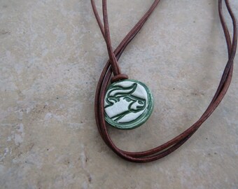 May include: A brown leather cord necklace with a green and white ceramic pendant featuring a bull's head design.