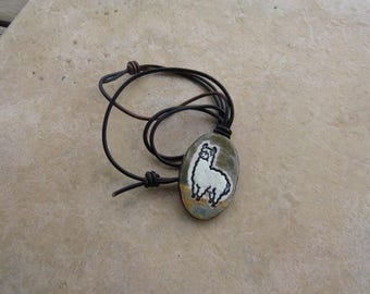 May include: Oval pendant necklace featuring a hand-painted white llama on a stone. The pendant is suspended from a black and brown leather cord with adjustable knots. The necklace is a unique, handcrafted accessory.