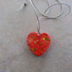 May include: A red heart-shaped pendant with yellow and orange speckles hangs from a simple string necklace.