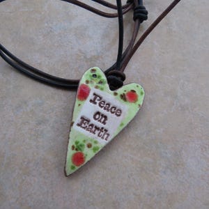 May include: A green heart-shaped pendant with red accents and the text "Peace on Earth" hangs from a brown leather cord.