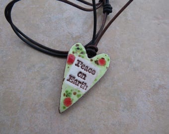 May include: A green heart-shaped pendant with red accents and the text "Peace on Earth" hangs from a brown leather cord.