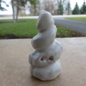 May include: White ceramic sculpture of a stacked rock formation with pink accents. The sculpture is a whimsical and abstract representation of nature.
