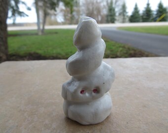 May include: White ceramic sculpture of a stacked rock formation with pink accents. The sculpture is a whimsical and abstract representation of nature.