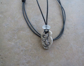 May include: A necklace with a white ceramic pendant featuring a carved floral design. The pendant is attached to a black leather cord.