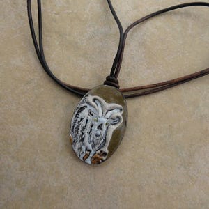 May include: A brown leather cord necklace with an oval pendant featuring a white ceramic goat with brown accents.