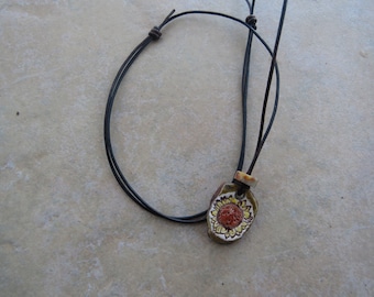 May include: A black leather cord necklace with a ceramic pendant featuring a yellow and red sunflower design.