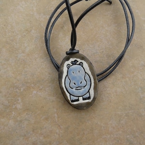 May include: A blue and white ceramic hippopotamus pendant on a black leather cord.