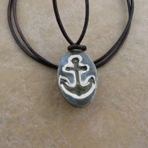 May include: A brown leather cord necklace with an oval pendant featuring a white anchor design on a blue background.