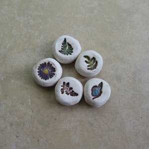 May include: Six white ceramic tiles with different floral and leaf designs. The designs include a purple flower, a green fern, a brown leaf, a blue butterfly, and two different green ferns.