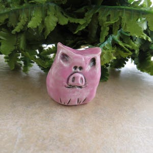 May include: A small pink ceramic pig figurine with a detailed face and snout.